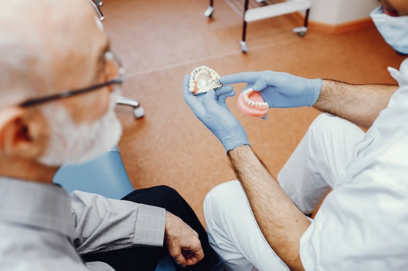Handsome old man talking to the dendist. Two men in the dentist&rsquo;s office. The doctor shows the patient dentures