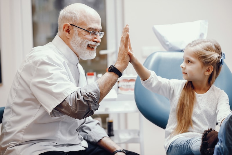 Little girl talking to the dendist. Child in the dentist’s office. Old man in a uniform